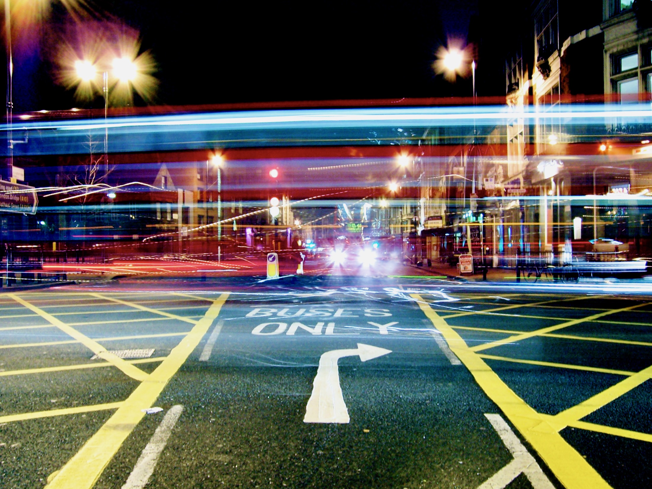 Vibrant trails of light streak across a busy street at night, illuminating the urban scene with a dynamic energy.