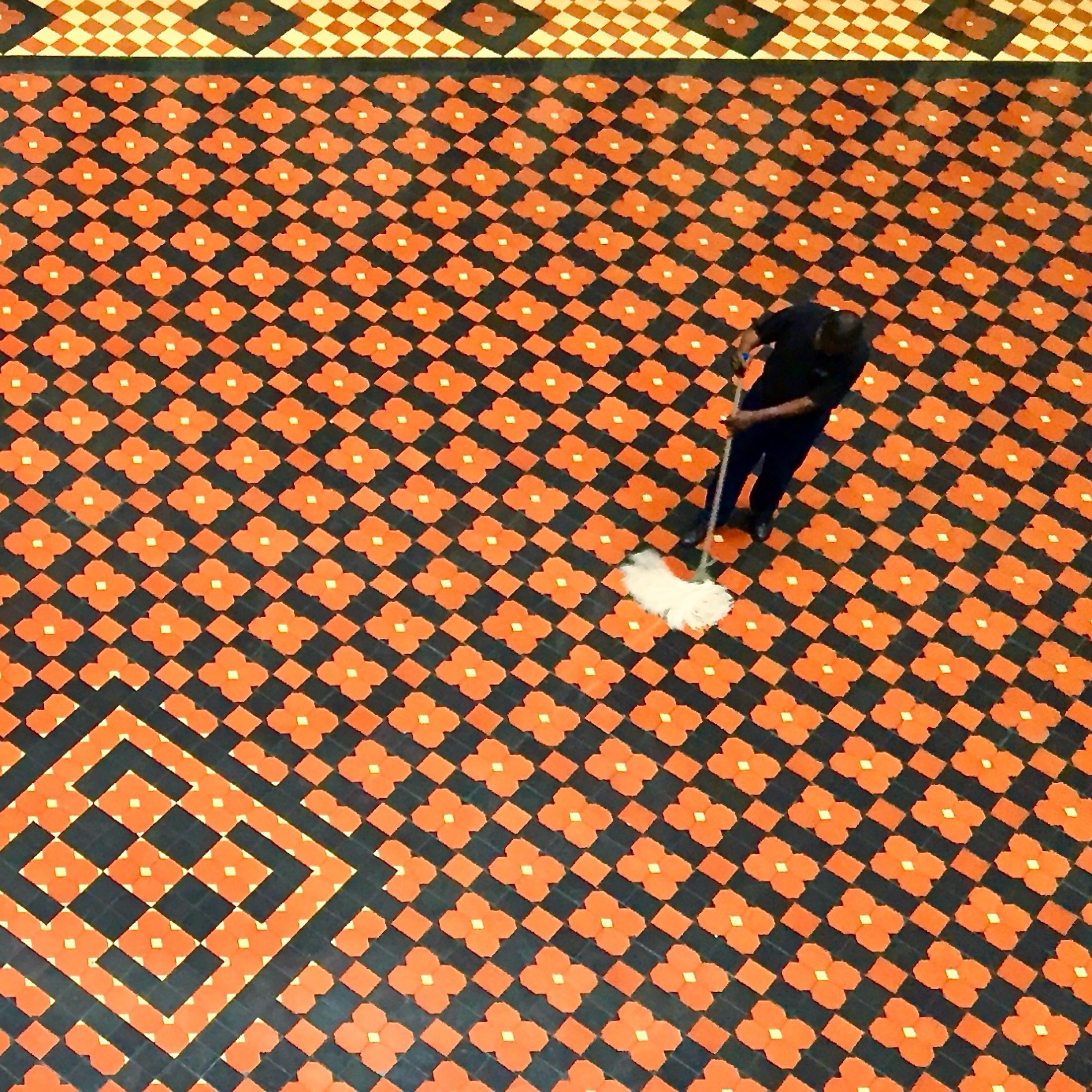 A lone figure mops a vibrant, patterned floor, creating a contrast of hard work against the striking geometric design.