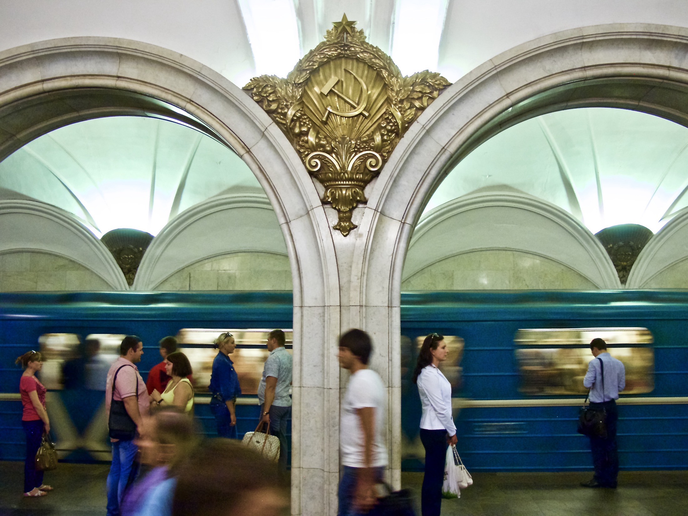 Swirling crowds await a subway train, framed by ornate arches that echo the historic Soviet grandeur of the underground station.