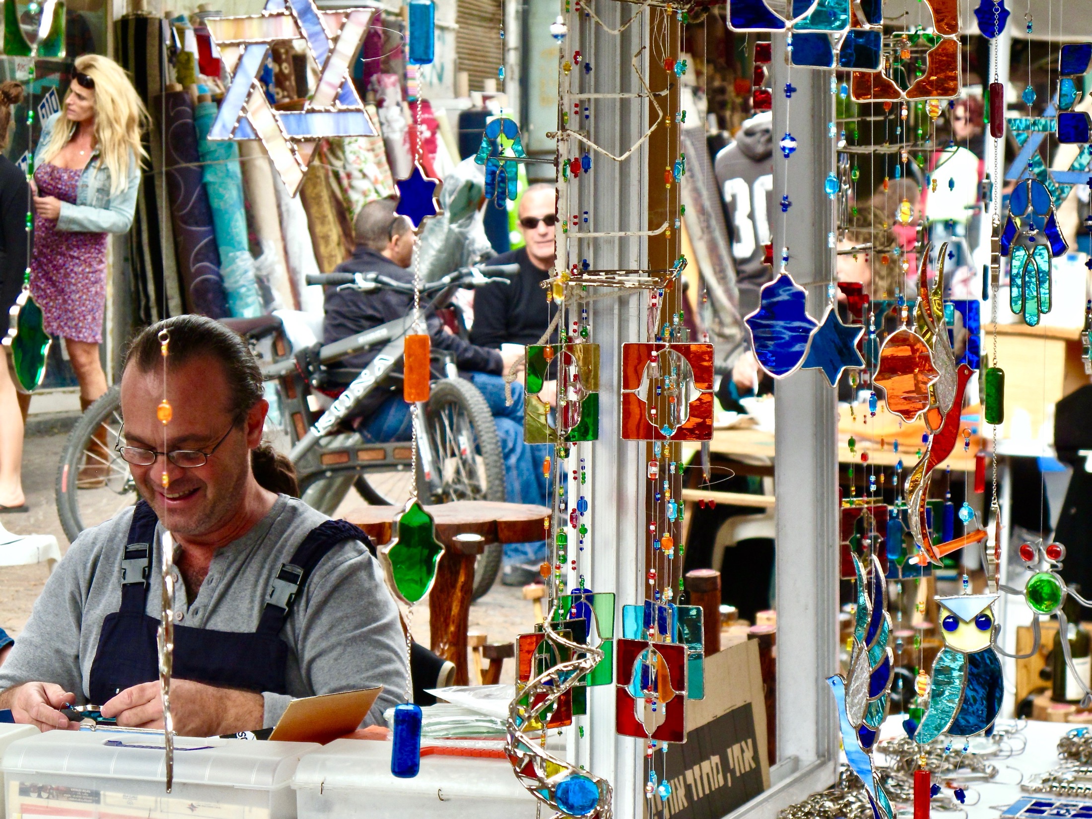 A smiling artisan crafts colorful glass ornaments, surrounded by bustling market life and vibrant decorations in the background.
