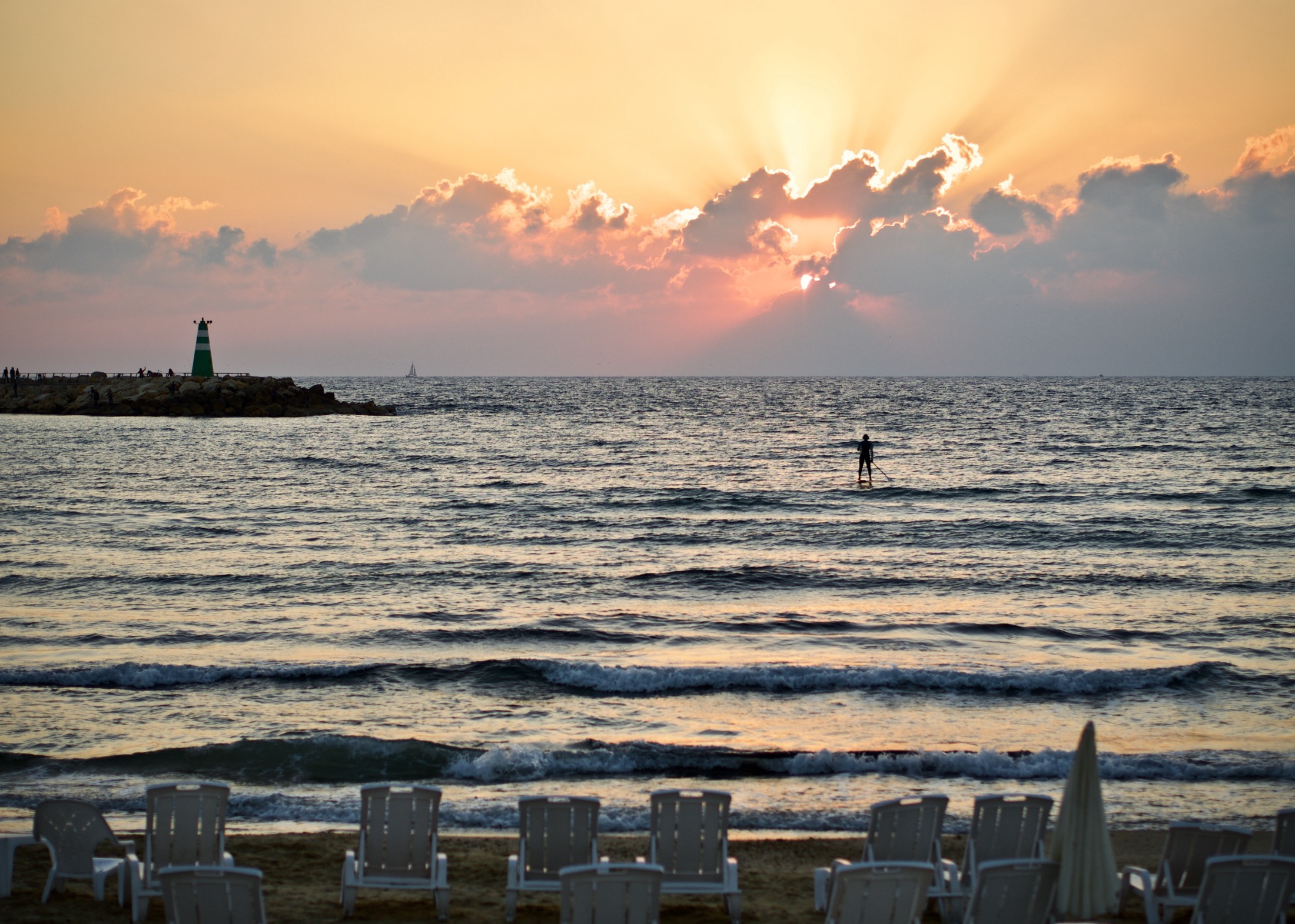 A silhouette of a paddleboarder glides across shimmering waves as a vibrant sunset paints the sky in warm hues.
